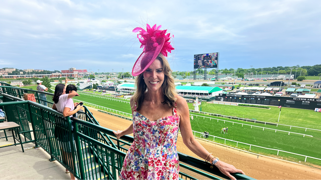 Woman wearing a pink fascinator and floral dress overlooking the Kentucky Derby racetrack.