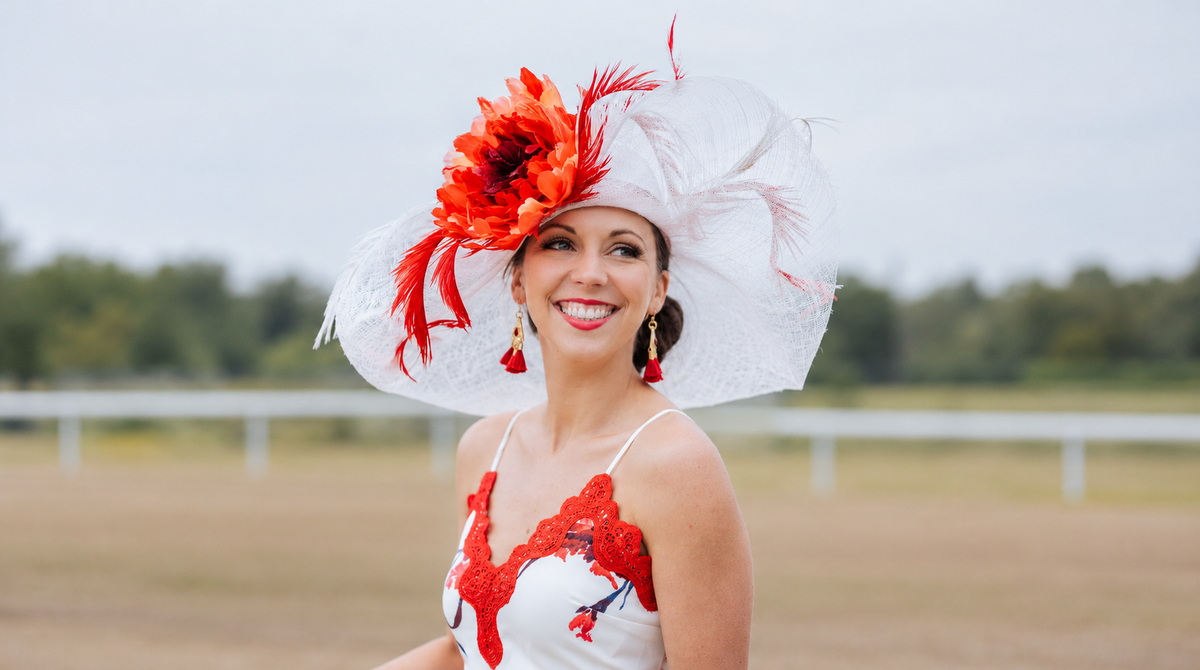  Smiling woman in a wide white Derby hat with red feather flower fascinator, a perfect Christmas gift for women who love hats.