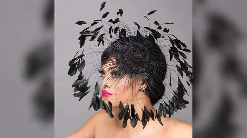 Woman wearing a black feather fascinator Halloween hat with lace rose detail and dramatic coque feathers and bright pink lips.