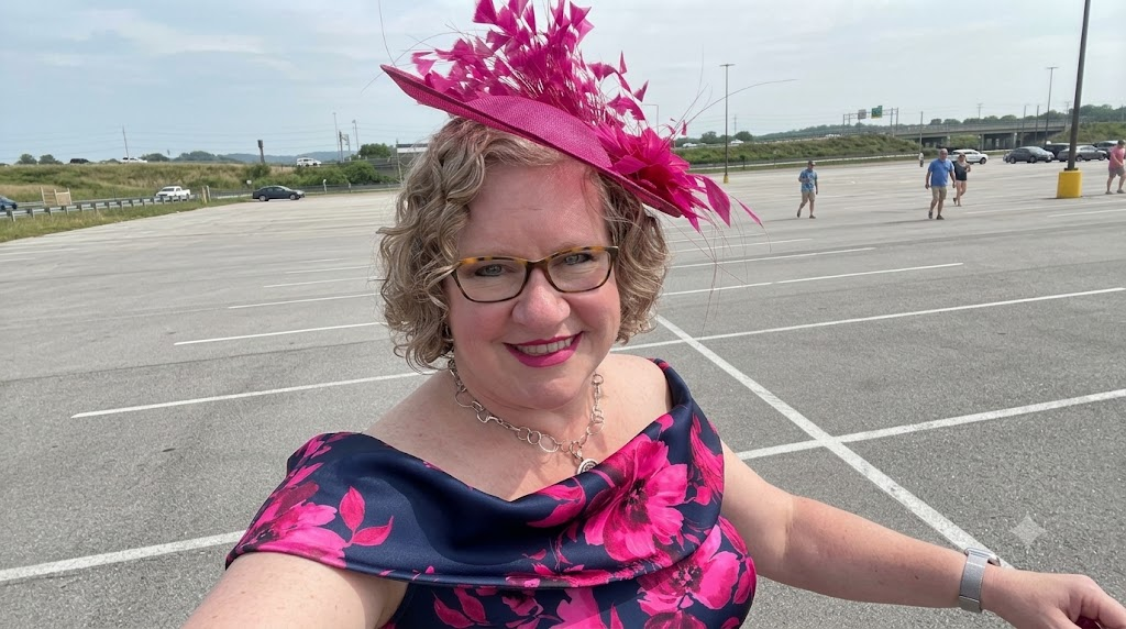 Smiling woman with curly hair wearing a magenta feather fascinator that stays secure, paired with a navy and pink floral gown.