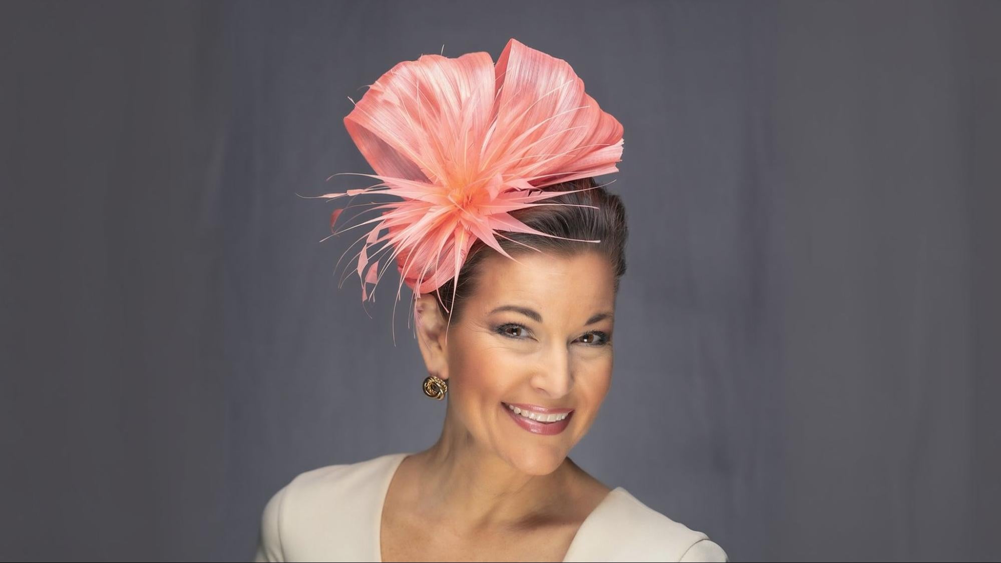 Woman wearing a coral pink feathered fascinator headpiece for Kentucky Derby